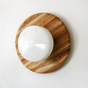 May include: A white glass light fixture with a round, frosted glass shade sits on a round wooden base with a natural wood grain.