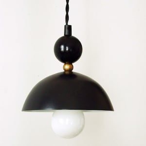 May include: A black pendant light with a round, dome-shaped shade and a black cord. The light has a white bulb and a gold accent.