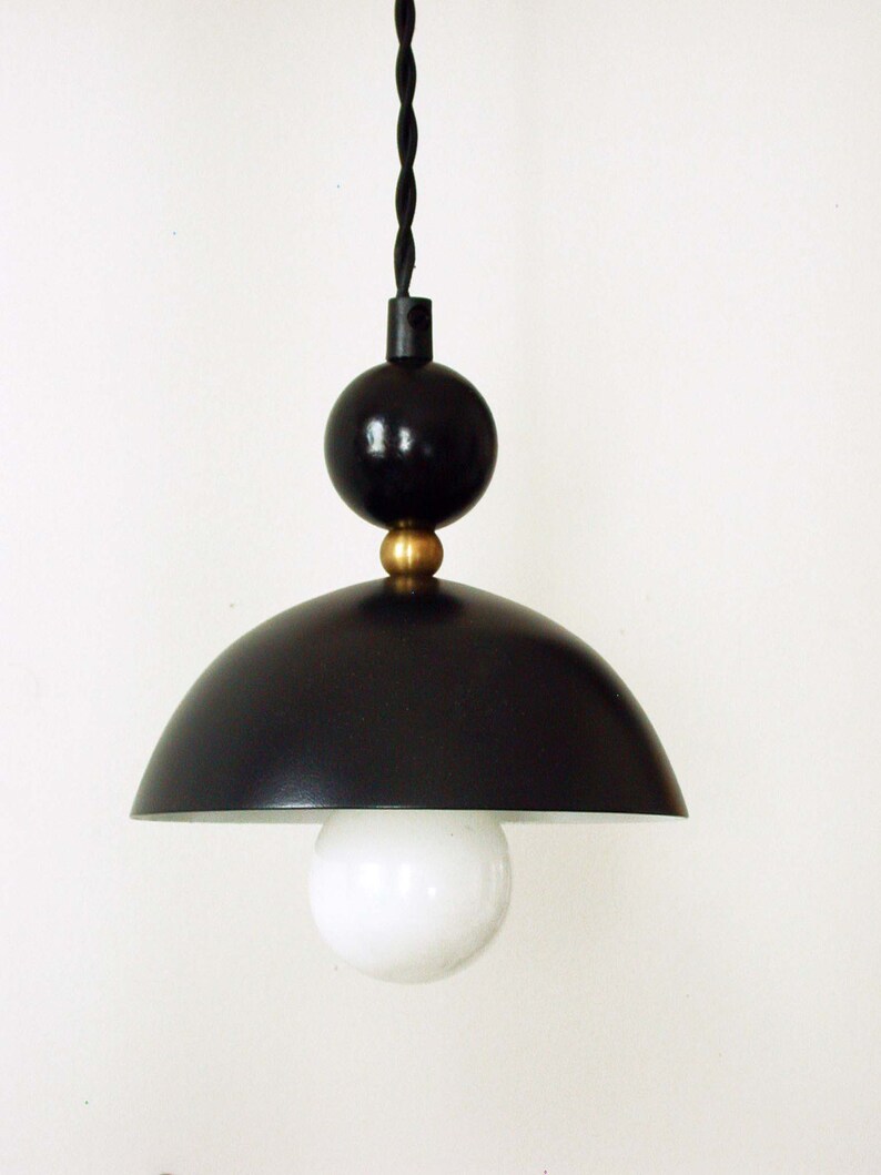 May include: A black pendant light with a round, dome-shaped shade and a black cord. The light has a white bulb and a gold accent.