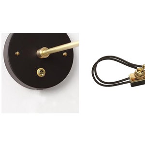 May include: A black and gold wall-mounted light switch with a round base and a long, thin arm. The switch is in the off position.