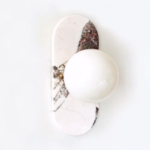 May include: A white marble wall sconce with a round white globe light fixture. The marble has pink and brown veins.