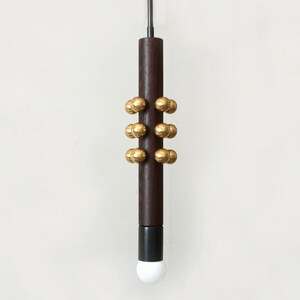 Puede incluir: Una lámpara colgante de madera oscura con un cable negro y una bombilla blanca. La lámpara tiene una serie de bolas de metal dorado alrededor del centro de la madera.