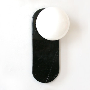 Puede incluir: Una lámpara de pared de mármol negro con una luminaria blanca en forma de esfera.