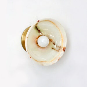 Puede incluir: Una lámpara de pared de mármol blanco y verde con base de latón y una bombilla blanca.