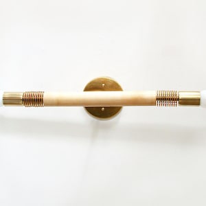 May include: A brass and wood wall sconce with two light bulbs. The sconce has a circular brass base and a long, thin wooden rod with a brass spring on each end.