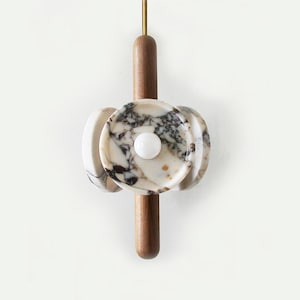 May include: A modern pendant light fixture with a wooden stem and three circular marble shades. The marble is white with brown and gray veins.