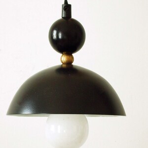 May include: A black pendant light with a round, white globe shade. The light has a black cord and a black metal base with a gold accent.