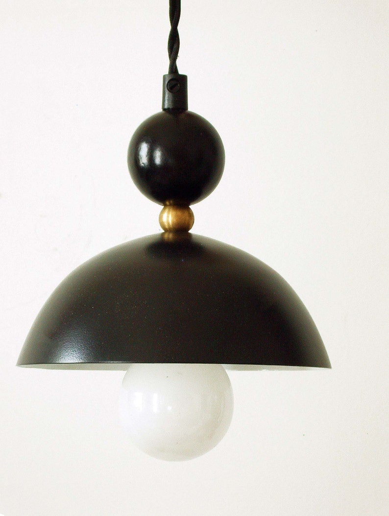 May include: A black pendant light with a round, white globe shade. The light has a black cord and a black metal base with a gold accent.