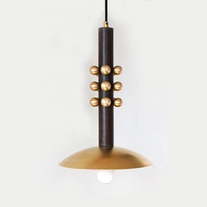 Puede incluir: Una lámpara colgante moderna con un cuerpo cilíndrico marrón oscuro adornado con seis esferas de latón. Una pantalla en forma de cuenco poco profundo, de color latón, está suspendida debajo, que alberga una sola bombilla. La luz cuelga de un cable negro.