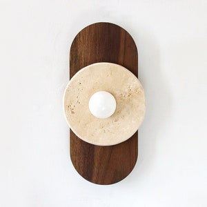 May include: A modern wall sconce with a round, light beige travertine stone shade and a walnut wood base.