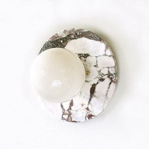 May include: A white marble wall sconce with a round, white glass shade. The marble has a pink and gray veining.
