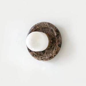 May include: A modern wall sconce featuring a round, marble-patterned base with a white, spherical light fixture. The sconce has a brass-colored ring around the light. The fixture is mounted on a white wall.