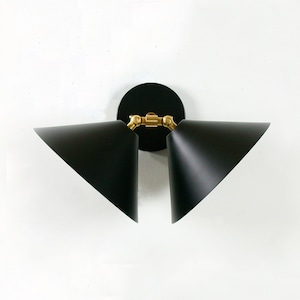 May include: A modern wall sconce with two black, triangular shades. The shades are angled and have white interiors. The fixture has a black circular base and brass-colored joints, creating a stylish lighting element.
