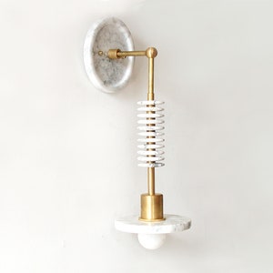 Puede incluir: Una lámpara de pared de mármol blanco y latón con un diseño en espiral único. La lámpara tiene una base redonda de mármol y un brazo de latón que se extiende hacia afuera para sostener una bombilla.