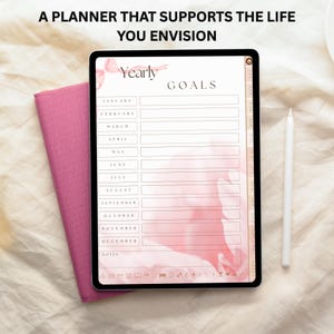 May include: A digital planner on a tablet with the text "A PLANNER THAT SUPPORTS THE LIFE YOU ENVISION." The planner displays "Yearly Goals" with sections for each month. A pink notebook and white stylus are next to the tablet.