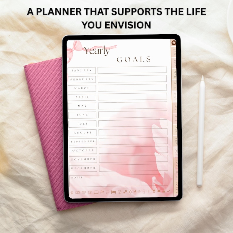 May include: A digital planner on a tablet with the text "A PLANNER THAT SUPPORTS THE LIFE YOU ENVISION." The planner displays "Yearly Goals" with sections for each month. A pink notebook and white stylus are next to the tablet.