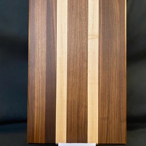 May include: A rectangular wooden chopping board with vertical stripes of light and dark wood. The board measures 50.8 cm long, 30.5 cm wide, and 3.8 cm thick. A small white card at the bottom has text.