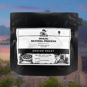 Puede incluir: Una taza de cerámica blanca con un asa negra y el texto "But First, Coffee" en un estilo manuscrito. La taza está sobre una superficie blanca. La taza mide 10 cm de alto.