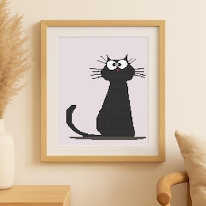 May include: Framed cross-stitch art featuring a black cat with large white eyes, whiskers, and a red nose. The cat is sitting on a gray line against a light pink background. The artwork is in a light brown wooden frame.