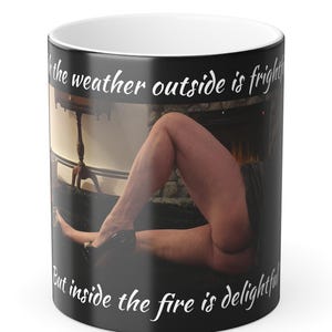 May include: A white ceramic mug with a black handle and the text "But First, Coffee" in a bold, black font. The mug is set against a blurred background, suggesting a cozy setting.