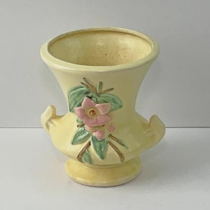 Może przedstawiać: Biały ceramiczny kubek z czarnym uchwytem i napisem "But First, Coffee" czarną, pogrubioną czcionką. Kubek stoi na białej powierzchni.