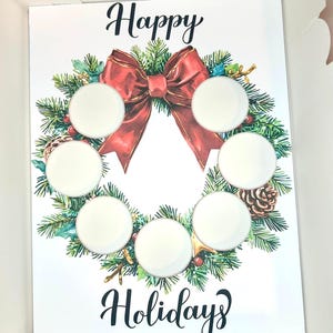 以下が含まれることがあります： お祝いのリースデザインの白いカード。リースは赤いリボン、緑の松の葉、黒い筆記体で「Happy Holidays」の文字が特徴です。7つの白い円がリースの内側に配置されています。