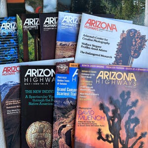 May include: A stack of vintage Arizona Highways magazines from the 1970s and 1980s. The covers feature colorful photographs of Arizona landscapes, including a desert scene with a Joshua tree, a Grand Canyon scene, and a Native American pottery design.