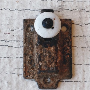 May include: A vintage, rusty metal door latch with a white porcelain knob. The knob has a black center and is slightly chipped.