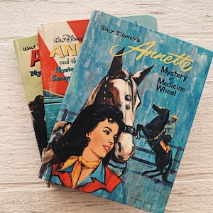 May include: Three vintage paperback books with a western theme. The front cover of the book on top features a girl with a horse and the text "WALT DISNEY'S Annette Mystery at Medicine Wheel". The middle book has the text "WALT DISNEY'S ANN and the Mystery Smugglers". The bottom book has the text "WALT DISNEY'S ANN and the Mystery Smugglers".