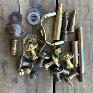 Pode incluir: Uma coleção de ferragens de latão antigo, incluindo botões, terminais, dobradiças e parafusos. As ferragens estão dispostas sobre uma superfície de madeira.