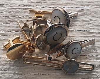 May include: A set of gold cufflinks and tie clips with a white enamel finish. The cufflinks and tie clips feature a letter 'C' and a design of the Eiffel Tower.