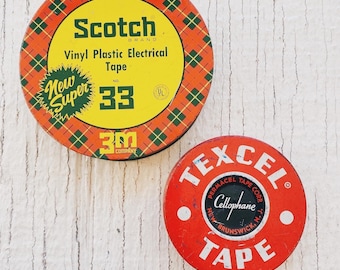 May include: Two vintage tape dispensers. One is red with the text "TEXCEL® PERMACEL TAPE CORP. Cellophane NEW BRUNSWICK, N.J. TAPE". The other is red, yellow, and green with the text "Scotch BRAND Vinyl Plastic Electrical Tape NO. 33 3M COMPANY UL".