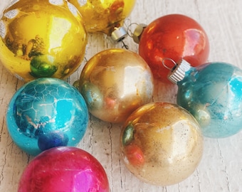 May include: A collection of vintage glass Christmas ornaments in various colors, including gold, red, blue, and pink. The ornaments are all round and have a shiny finish.