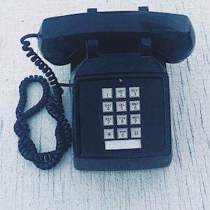 May include: A black rotary phone with a push-button keypad. The phone has a black coiled cord and a black receiver.
