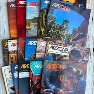 May include: A stack of vintage Arizona Highways magazines from the 1970s. The covers feature colorful illustrations of desert landscapes, Native American art, and southwestern scenery. The magazines are in good condition and would be a great addition to any collector's library.