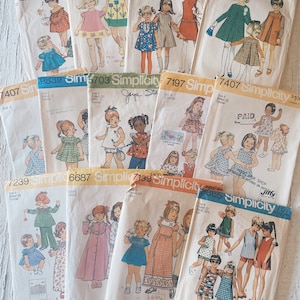 May include: A collection of vintage Simplicity sewing patterns for children's clothing. The patterns feature a variety of styles, including dresses, skirts, pants, and tops. The patterns are printed on paper and have illustrations of the finished garments.