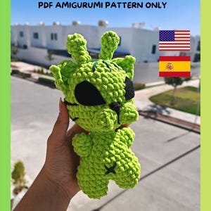 Puede incluir: Un amigurumi de gato alienígena verde tejido a ganchillo con un parche en el ojo negro y una X cosida en el pecho. El texto "GATO ALIEN / ALIEN CAT PDF AMIGURUMI PATTERN ONLY" está en la imagen.