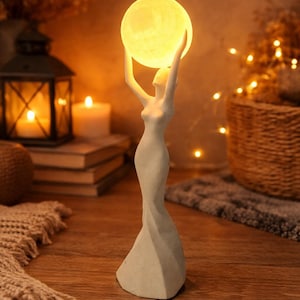 May include: A decorative figurine of a woman holding a glowing orb overhead. The figure is in a flowing gown, and the orb emits a warm, soft light. The statue is on a wooden surface, with candles and a lantern in the background.