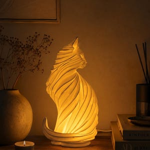 May include: A white, sculptural cat-shaped lamp with a swirling, ribbed texture that emits a warm, soft glow from within. The feline figure is depicted in a seated profile position with its tail curved gracefully along the base.