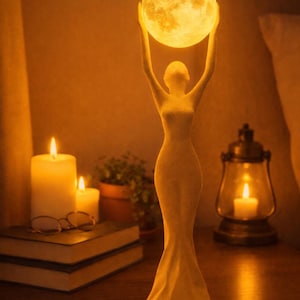 May include: A cream-colored sculpture of a woman holding a glowing moon-shaped light above her head. The lamp is on a wooden nightstand with candles, books, and a lantern. The overall theme is a warm, inviting ambiance.