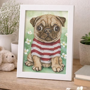 Può includere: Un punto croce incorniciato di un carlino con una maglietta a righe rosse e bianche. Il carlino è seduto su uno sfondo verde con fiori bianchi. La cornice è bianca.