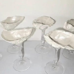 May include: Six champagne glasses with oyster shell-shaped bowls in pearly white. The clear stems and round bases add to the elegant design. A unique set for special occasions.