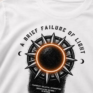 May include: A white t-shirt featuring a black and orange graphic of a solar eclipse surrounded by spikes. The text reads A BRIEF FAILURE OF LIGHT, TEMPORARY COLASTIAL INTERRUPTION, OBSERVATION RETORD, and 12.08.2026, with small crescent moons on the sides.