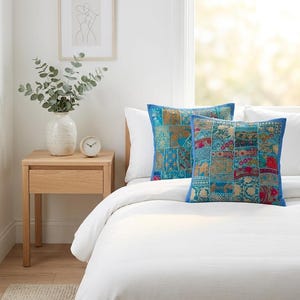 May include: Two square throw pillows featuring a vibrant patchwork design in shades of blue, teal, gold, and red. The pillows are decorated with intricate embroidery and metallic thread accents, finished with a solid blue border on all four sides.