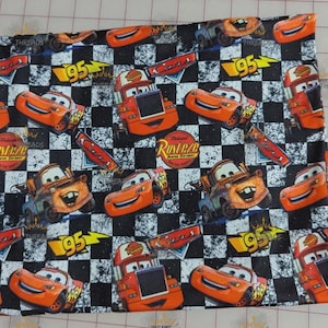 May include: Fabric with a repeating pattern of orange race cars, the number 95, and other graphics on a black and white checkered background. The fabric has a Cars theme.