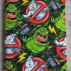 May include: Fabric with a repeating pattern of green and white ghosts, red no-ghost symbols, and proton packs on a dark green background. Yellow lightning bolts and the text "THREE KINGS THREADS" are also visible.
