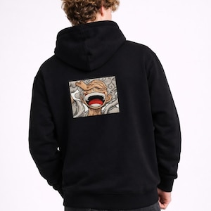 May include: Black hooded sweatshirt featuring a colorful graphic on the back. The graphic is a cartoon image of a character with a wide open mouth and a hand over the eye. The sweatshirt has a drawstring hood and long sleeves.