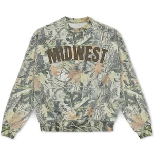May include: A long-sleeve crewneck sweatshirt featuring a camouflage pattern of tree bark and autumn leaves in shades of green, brown, and tan. The word MIDWEST is printed in large, dark brown, arched capital letters across the chest area.