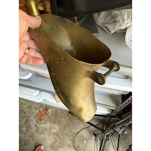 May include: A vintage brass scoop with a handle. The scoop has a curved shape and a wide opening. The handle is attached to the side of the scoop with a small decorative element. The brass has a warm, aged patina.