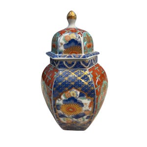 Pode incluir: Um pote de gengibre de cerâmica com tampa e remate dourado. O corpo é decorado com um padrão vibrante de motivos florais em laranja, azul e branco, linhas geométricas e detalhes dourados sobre a sua estrutura hexagonal e arredondada.